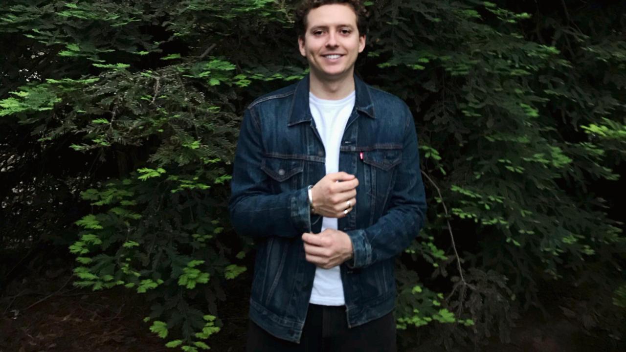 Austin Dalmasso in blue button up shirt with dark green tree background