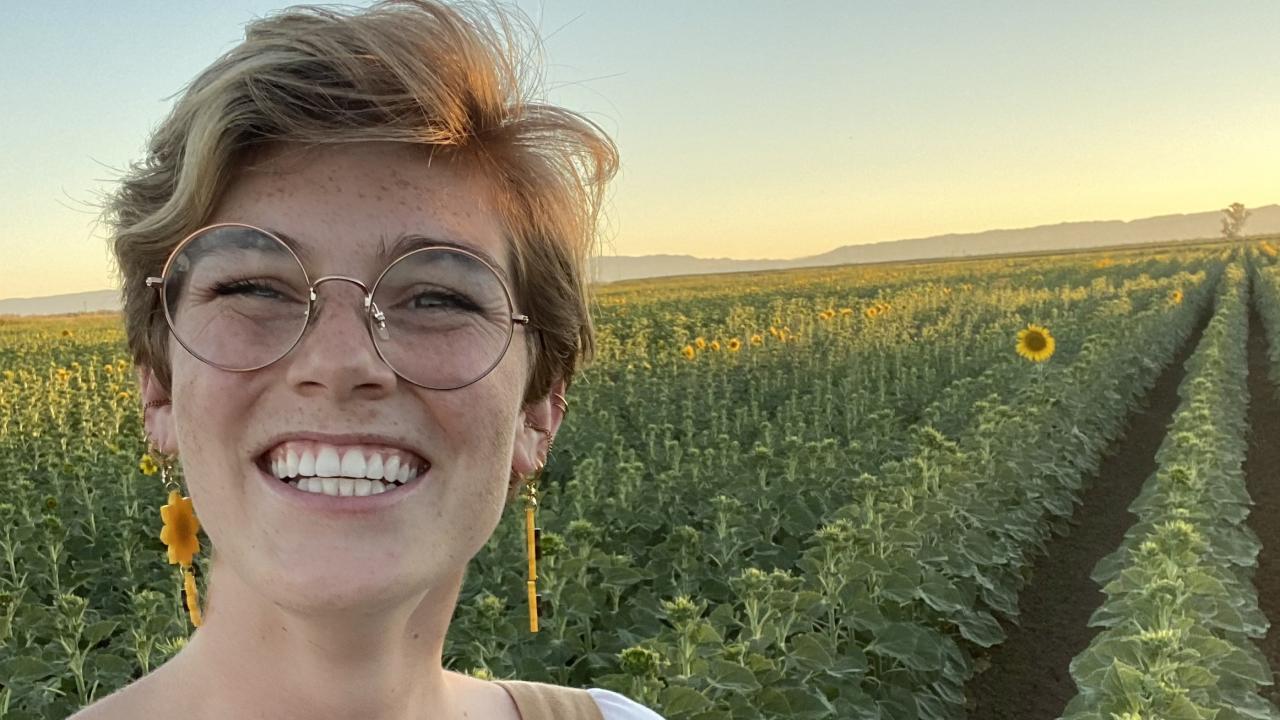 elizabeth roth smiling at the camera wearing overalls in a field at sunset