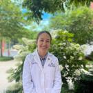 Hana Minsky in a white Johns Hopkins lab coat smiling with greenery in the background