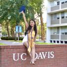 Anjolie Doan sitting on UCD sign, grad photo