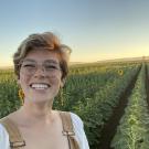 elizabeth roth smiling at the camera wearing overalls in a field at sunset