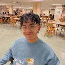 robert chin smiling at the camera wearing a duck sweater and sitting in the library